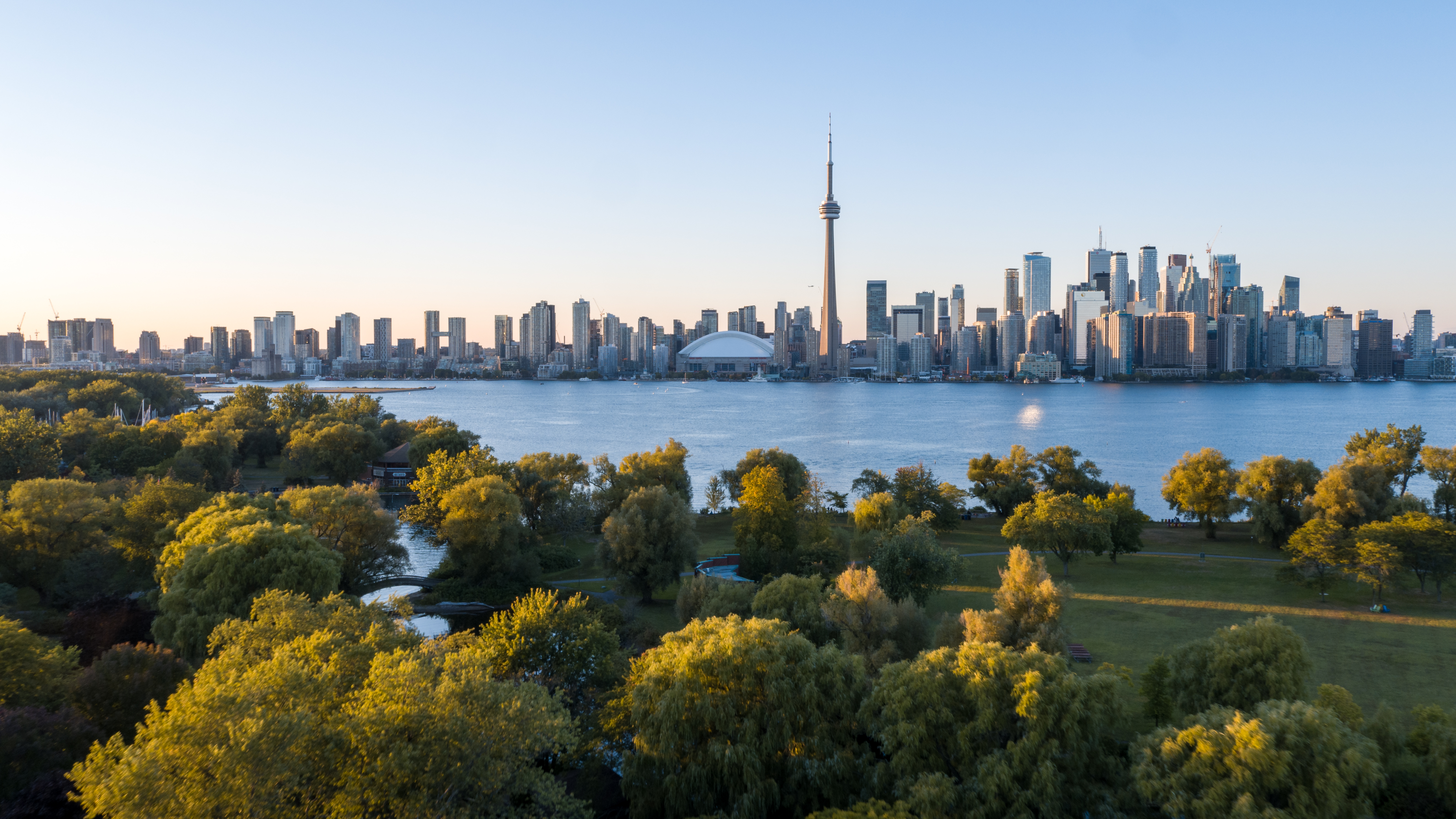 Toronto’s city skyline is across from Lake Ontario and a green park with trees  