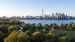 View of Toronto's skyline overlooking a park with trees and Lake Ontario.