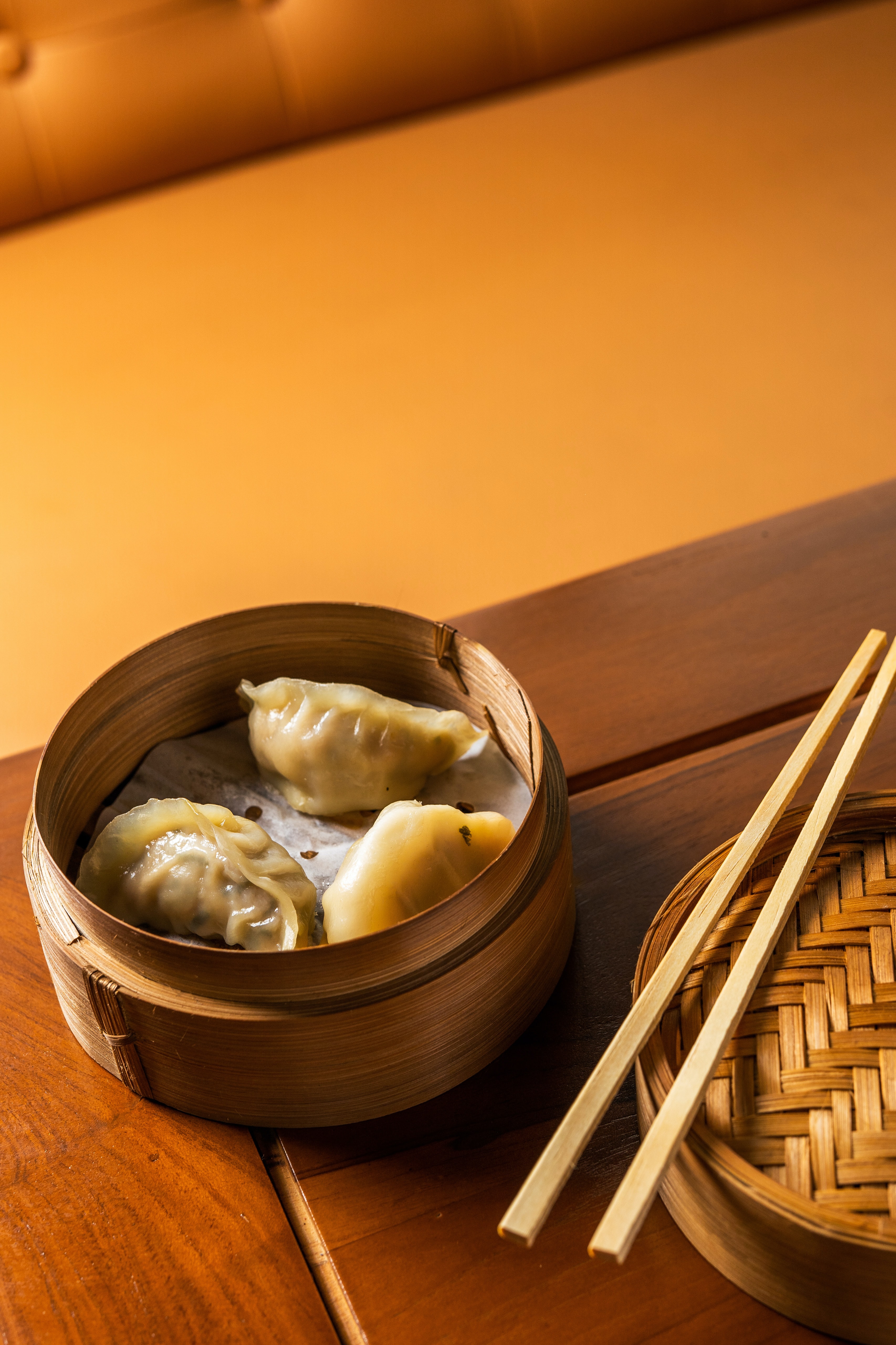 Close up of dumplings in a bamboo serving basket and chopsticks on the side