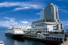 Pan Pacific Hotel towers over Vancouver harbour. A cruise ship is docked nearby.