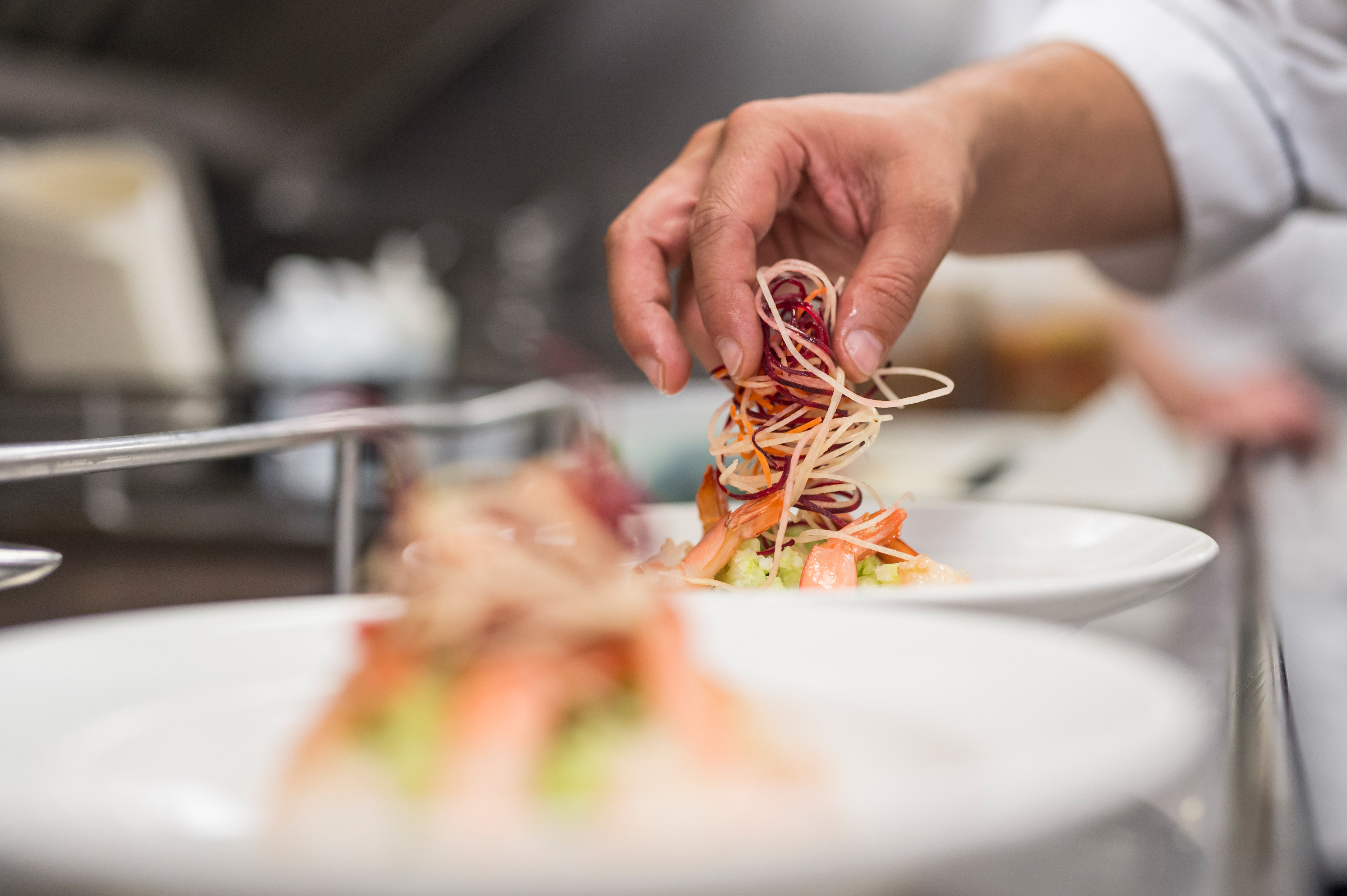 A dish of pacific prawns being garnished by a cook