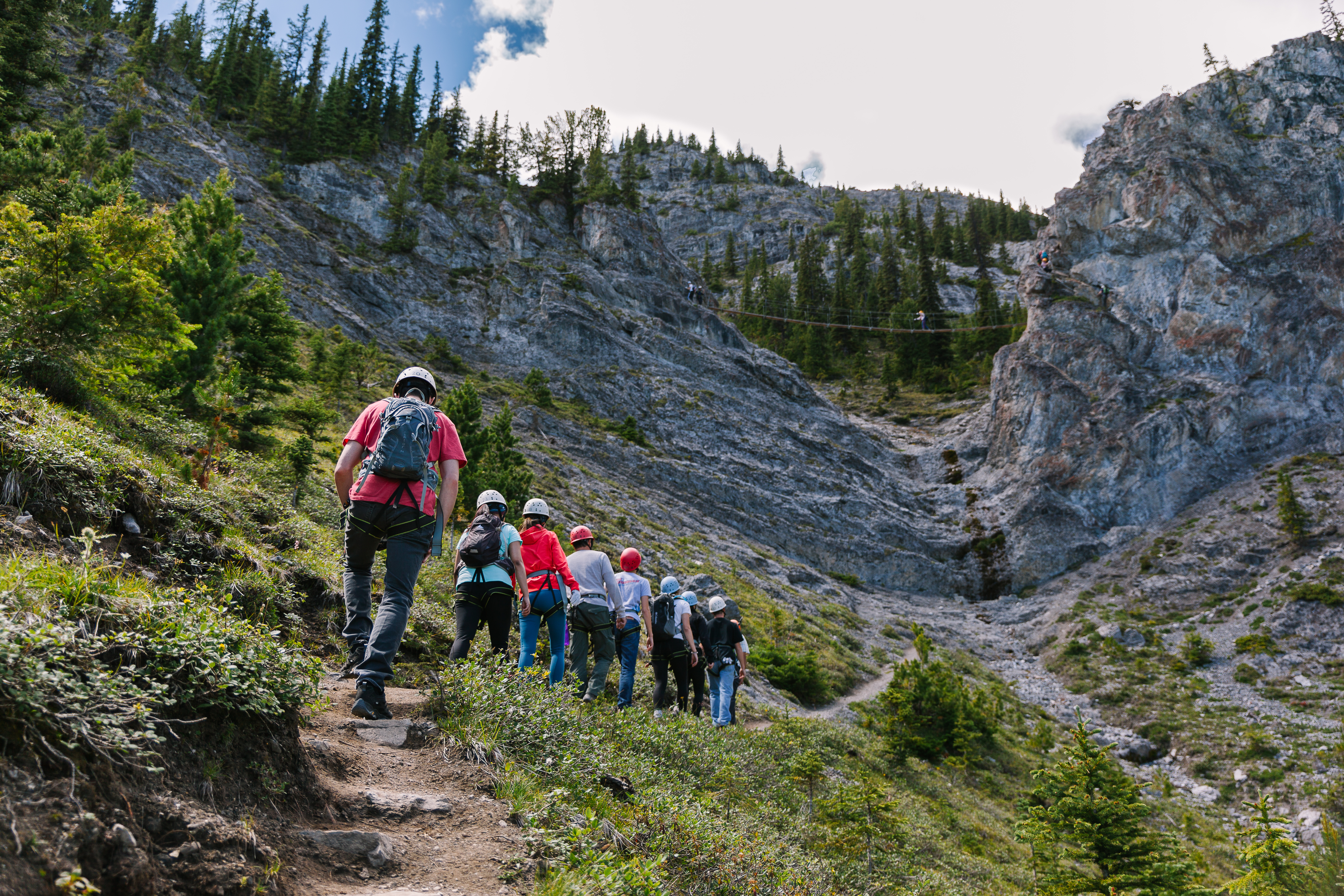 Hikers on a guided tour walk up mountain trail with a suspension bridge in view above