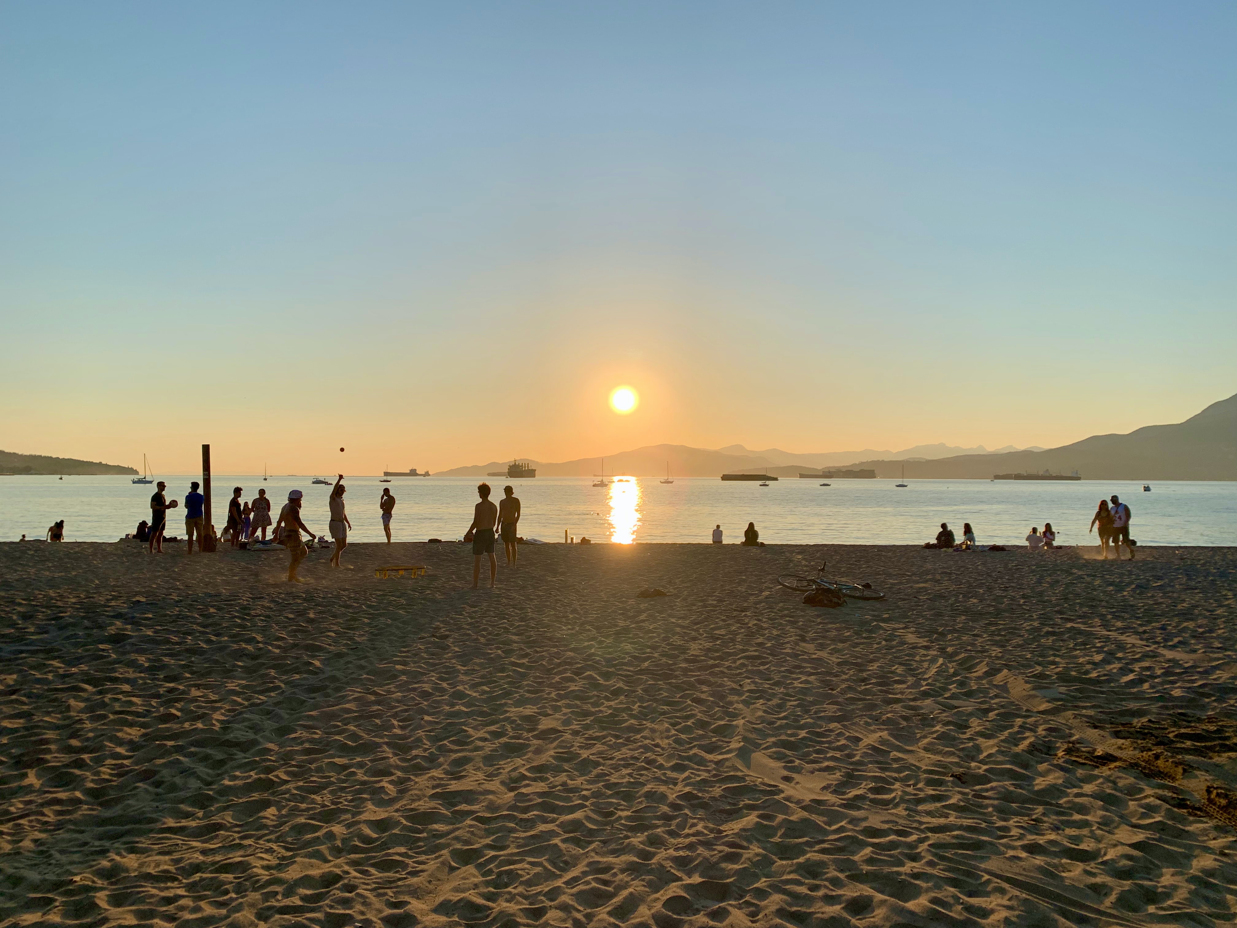 People on Vancouver's sandy Kitsilano beach at sunset faces mountains and English Bay