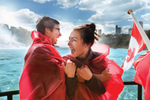 Two people laugh while wearing red ponchos in front of Niagara Falls