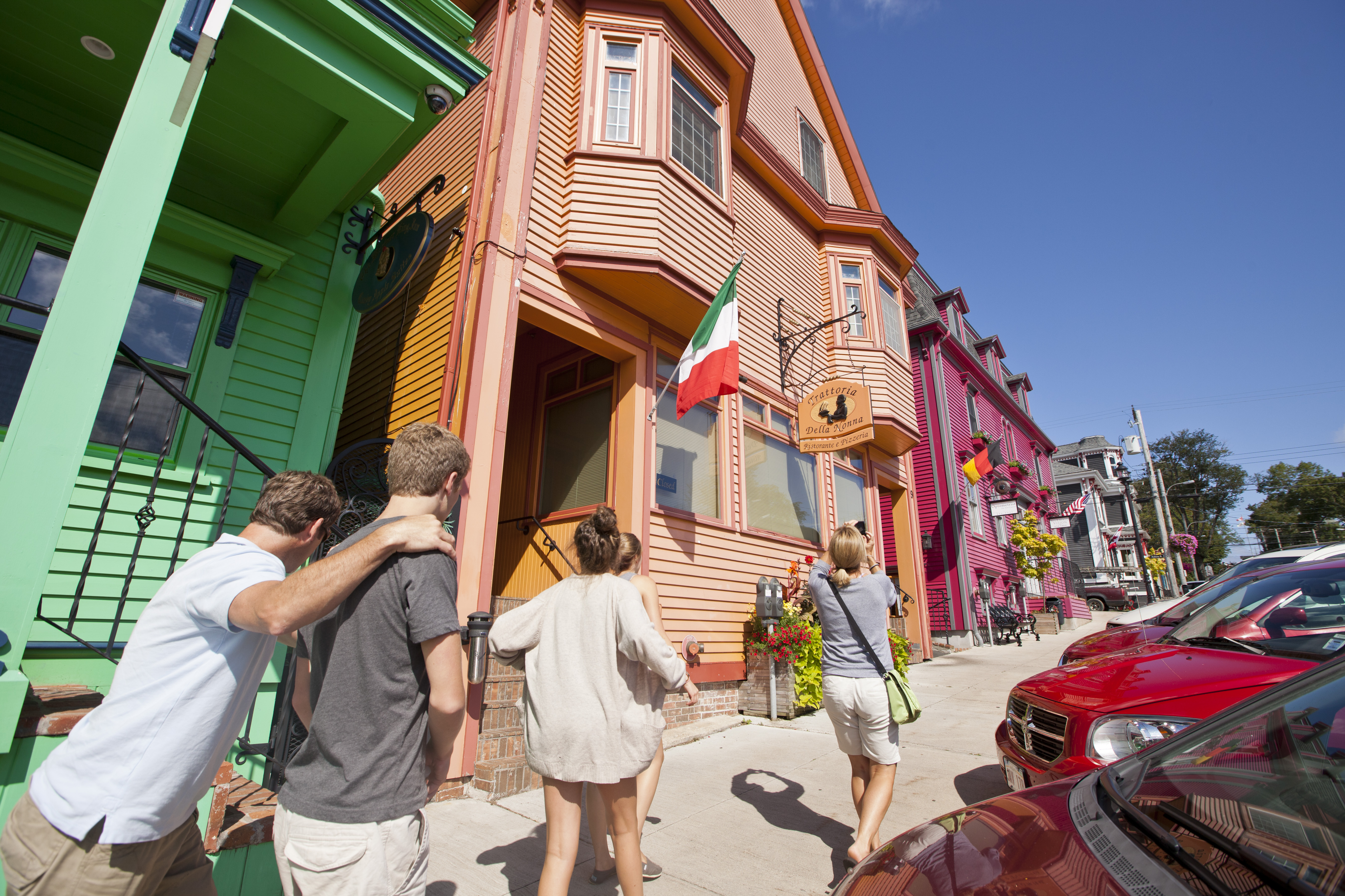 A group walk on a street with a row of colourful buildings contrasted by a blue and clear sky above