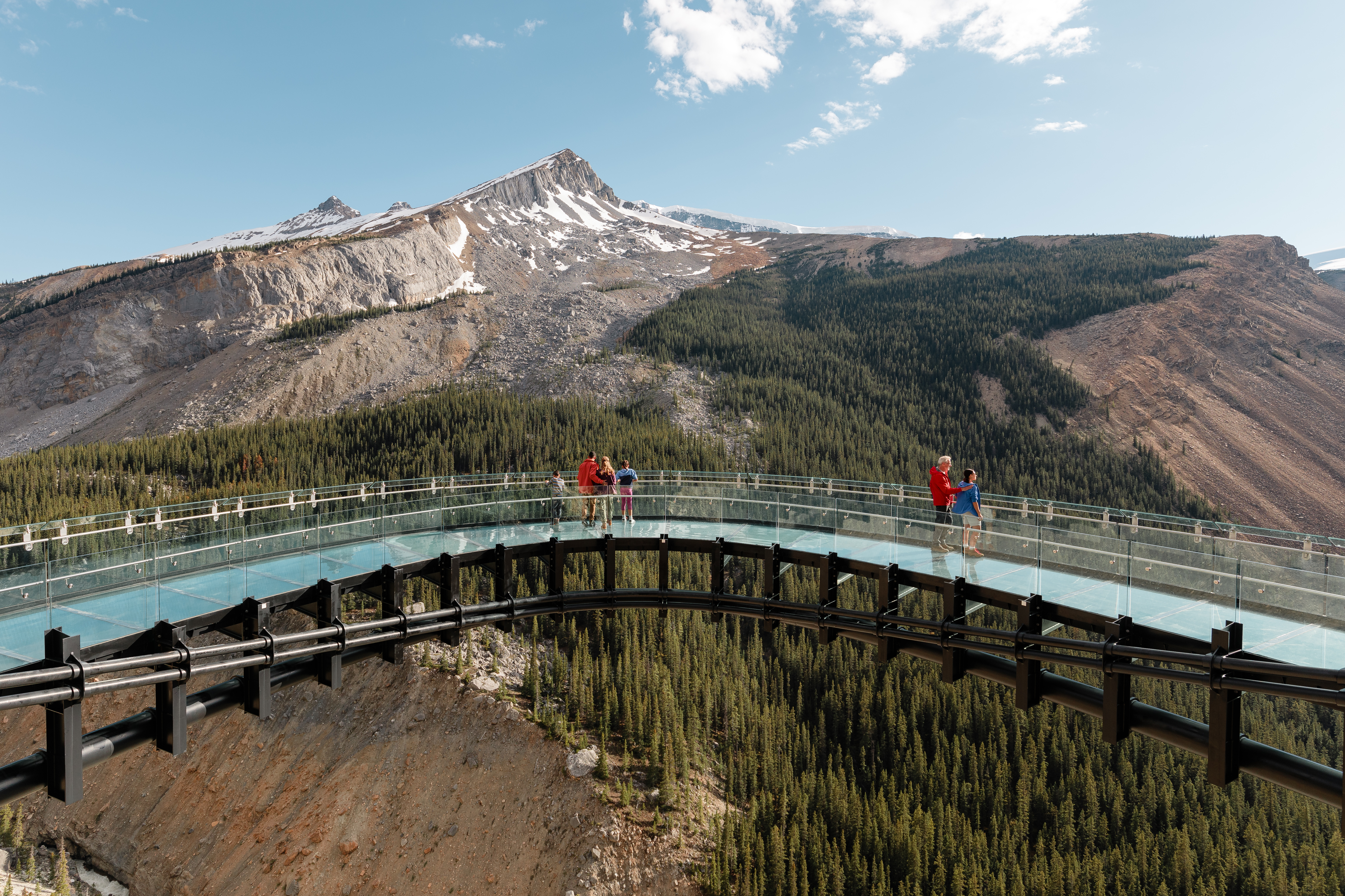Visitors take in expansive view of mountain peaks against a blue and clear sky from observation platform