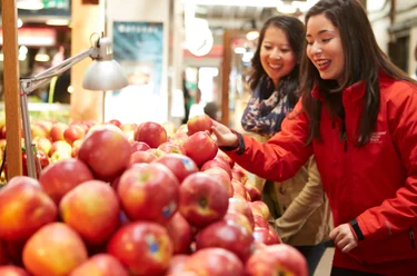 two people look at a pile of apples in a market