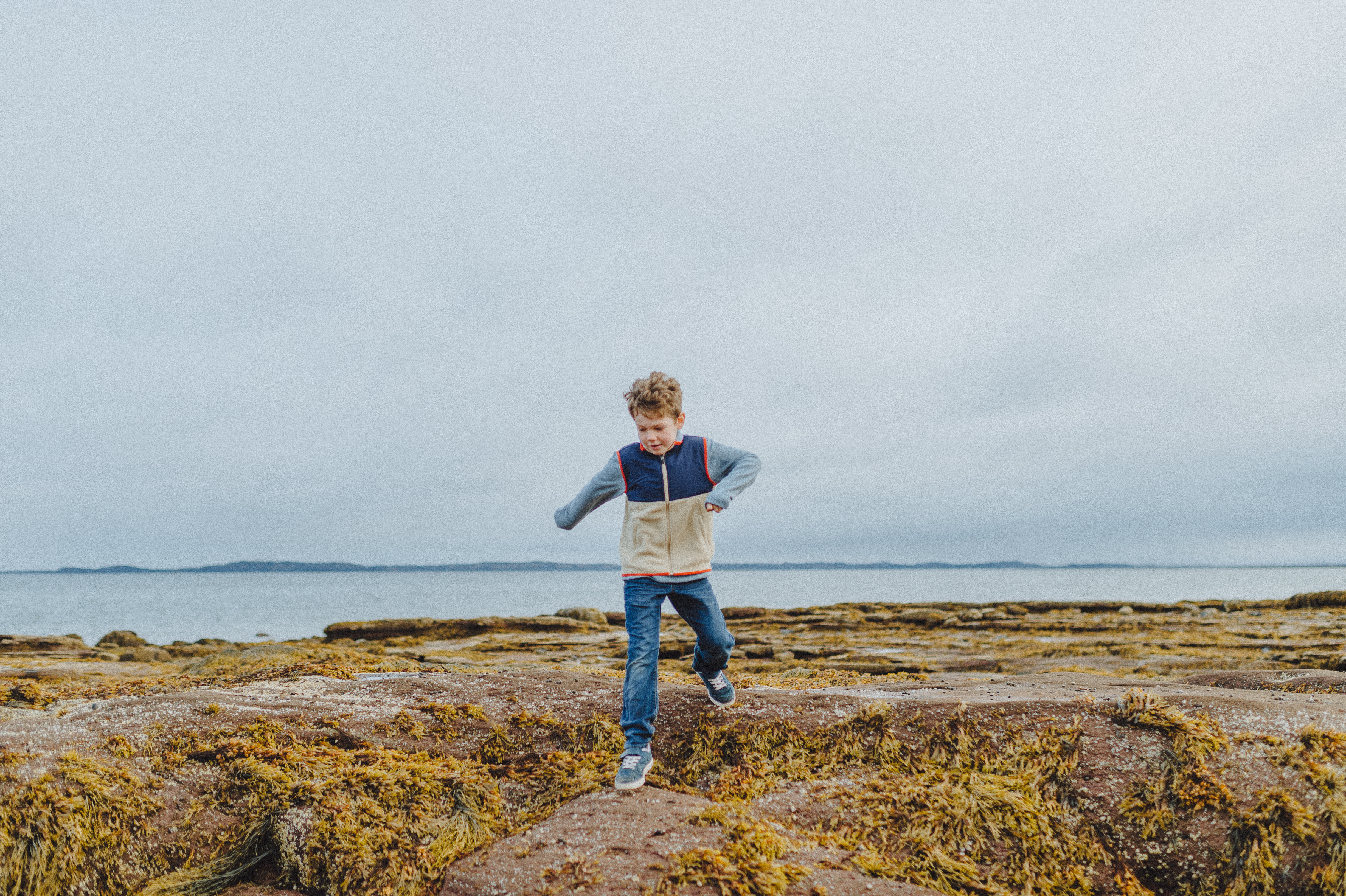 Young boy leaps on ocean floor at low tide in, Ministers Island, a National Historic Site of Canada near Saint Andrews