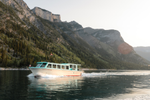 Boat travels through open waters in Lake Minnewanka and beside forested slopes