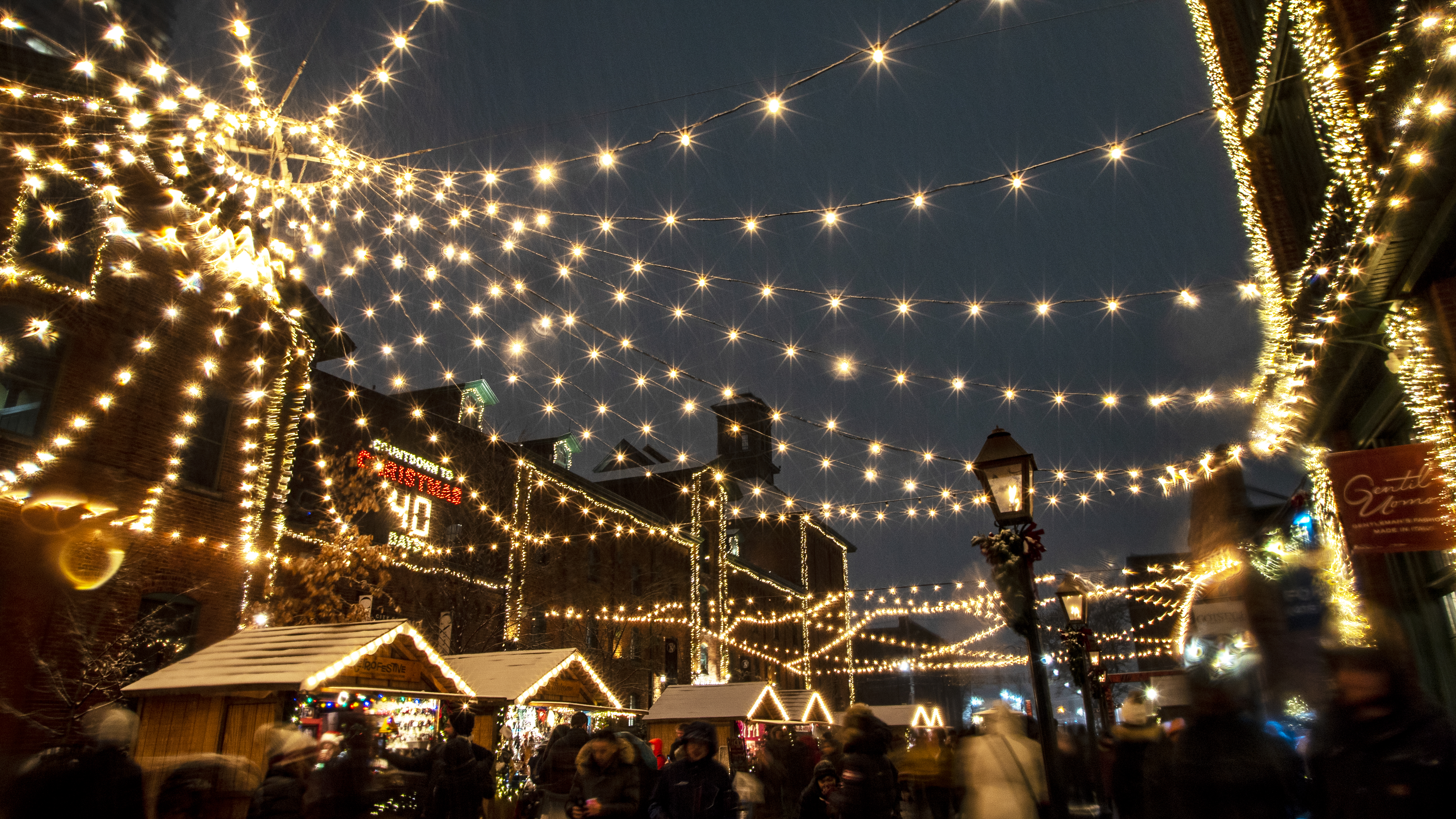 Strings of lights above Christmas market stalls at night