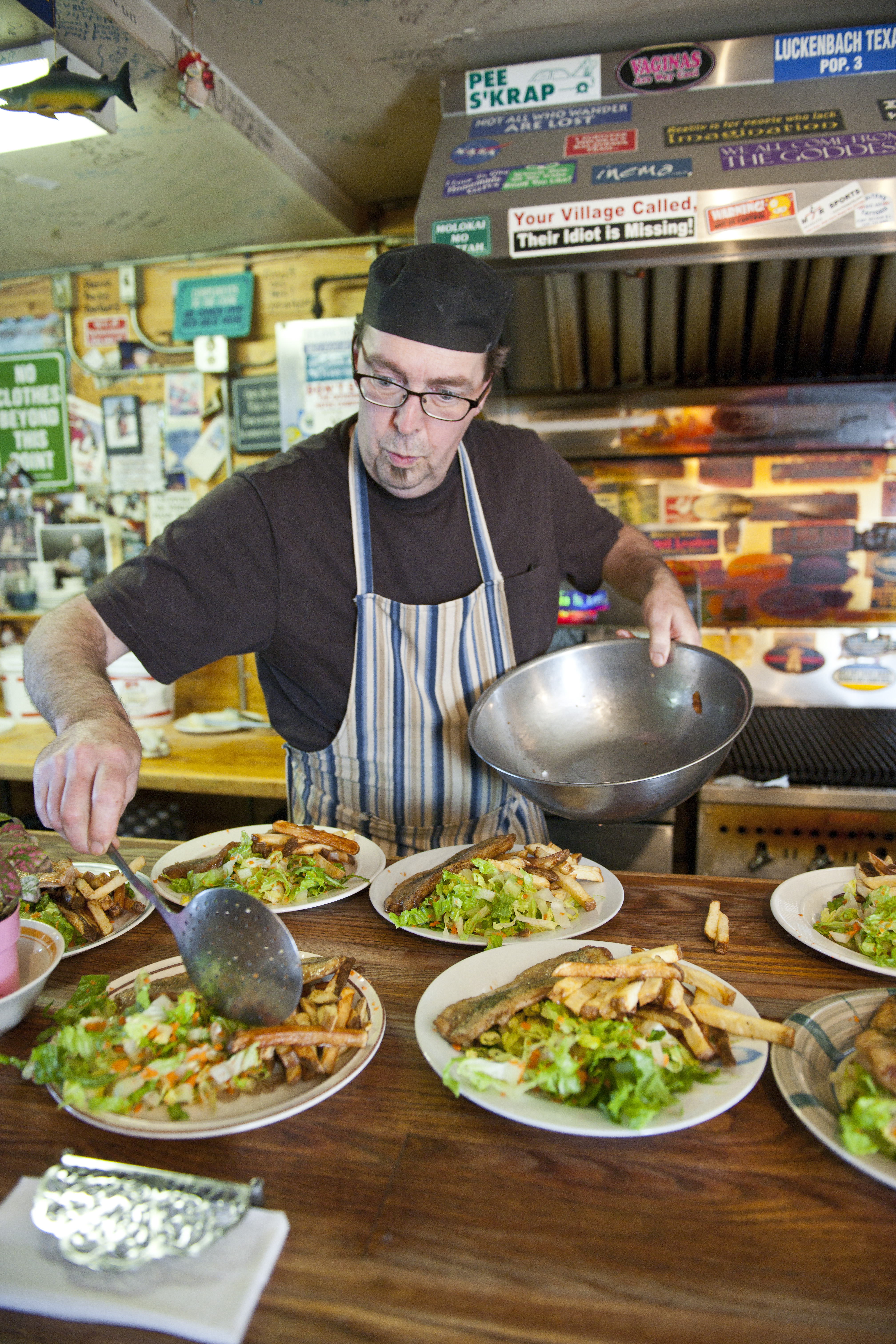 Cook at work in the kitchen puts final touches to dish with multiple servings placed in front of him 