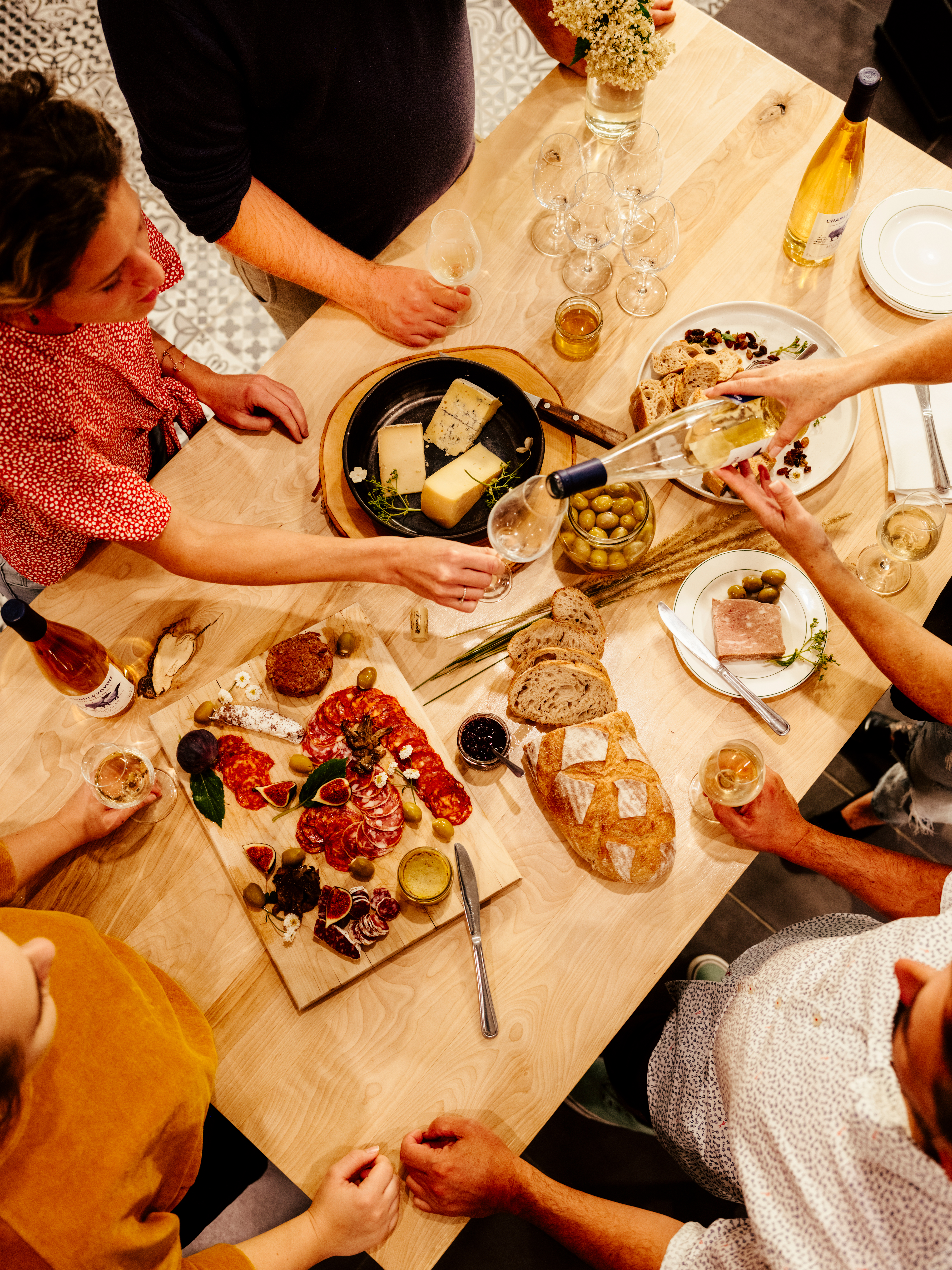 Small group gather around a table to feast on cheeses and charcuterie 