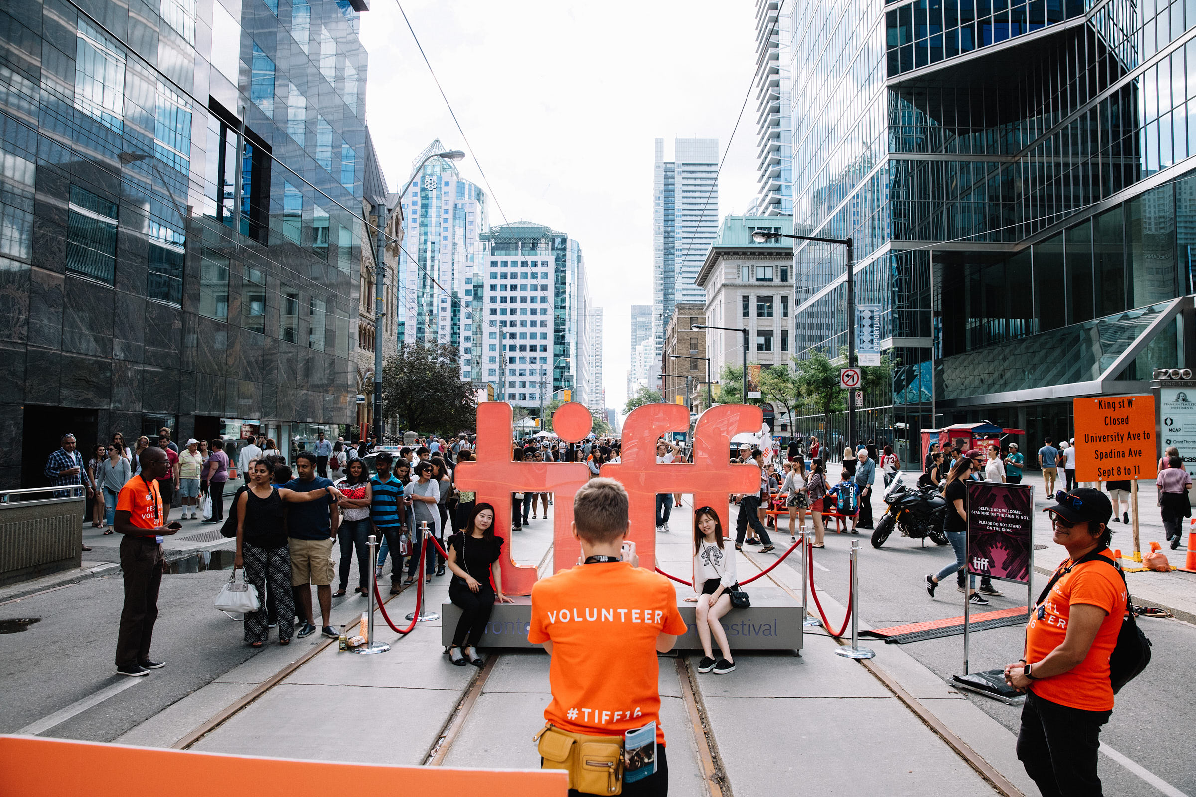 A volunteer takes a photo of two people in front of a Toronto International Film Festival sign