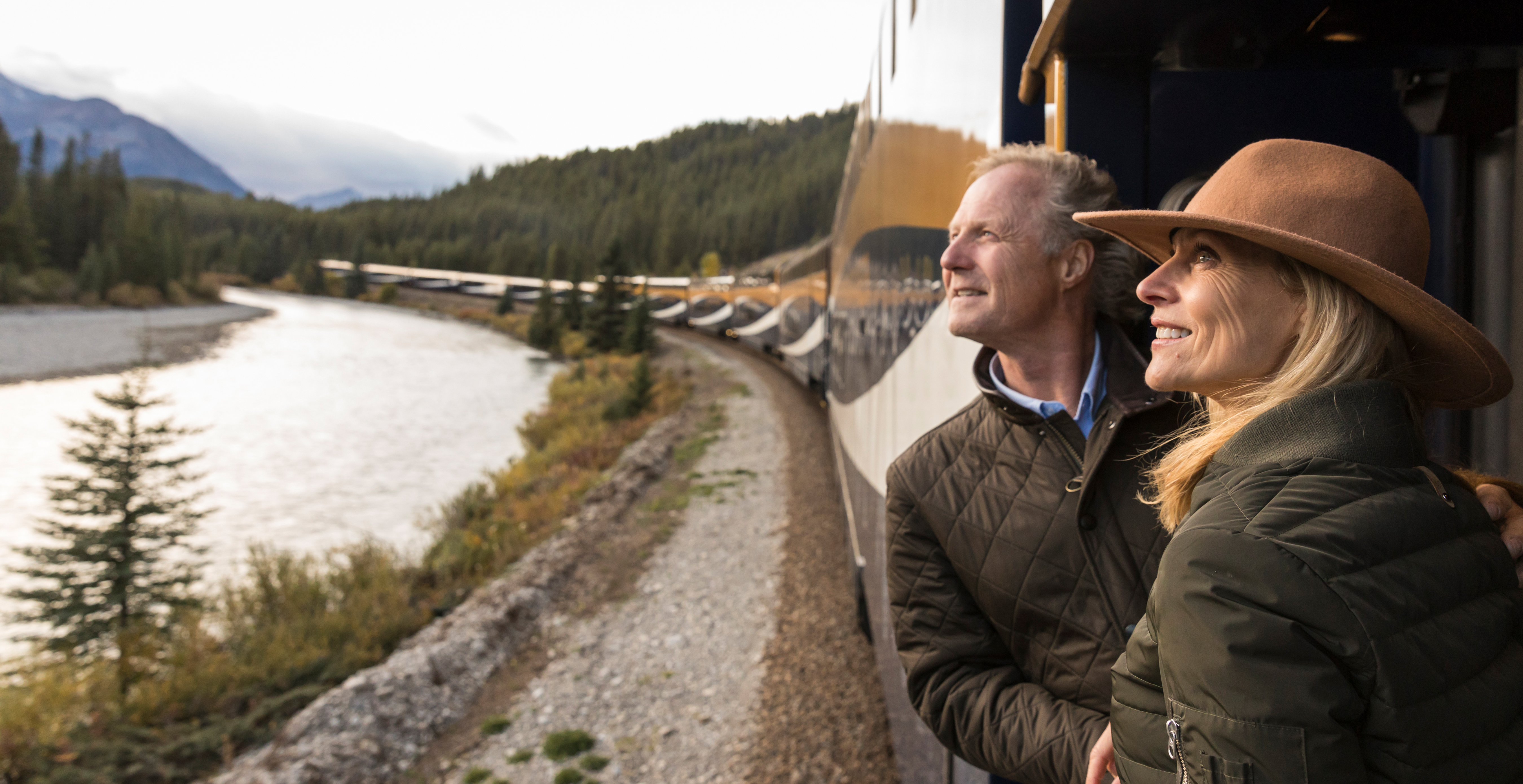 Two people look at the Rocky Mountains from the Rocky Mountaineer outdoor viewing platform 