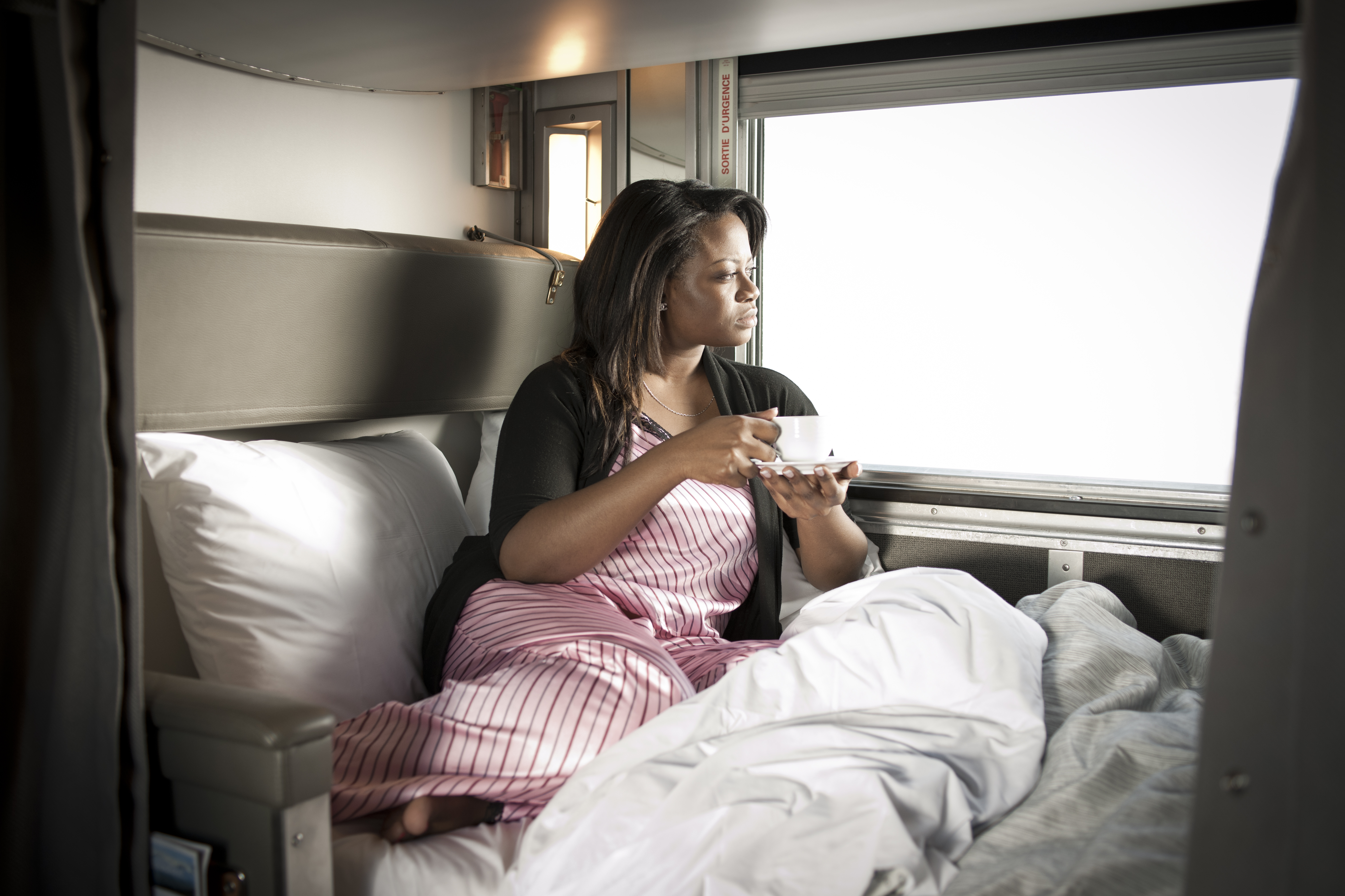 A woman peers out the window of her VIA cabin with a coffee cup in hand
