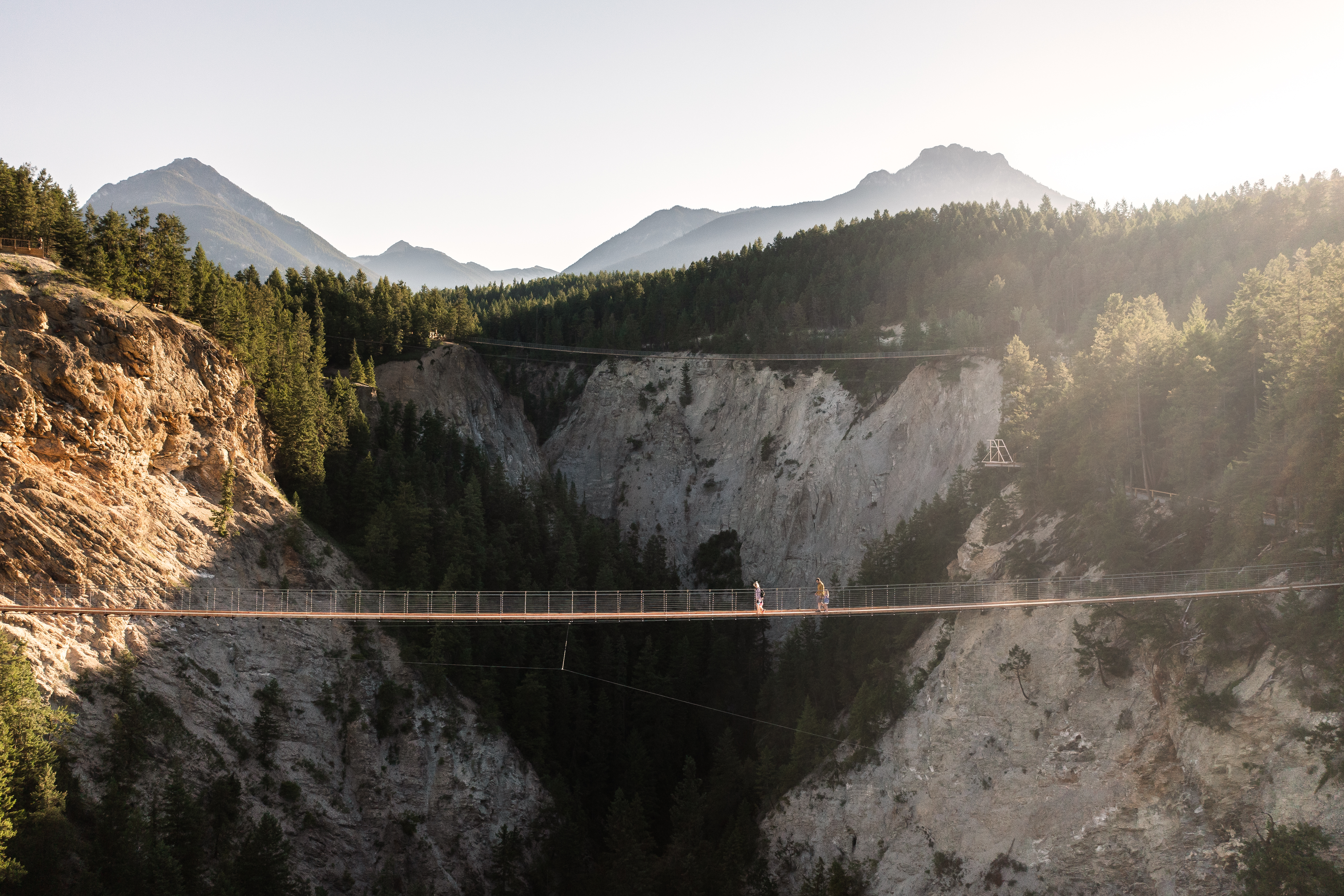 Family of four walks past mountain views on long suspension bridge located above Columbia Valley in the Kootenay Rockies