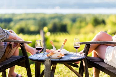 A couple sisters overlooking a vineyard while drinking wine, bread and cheese