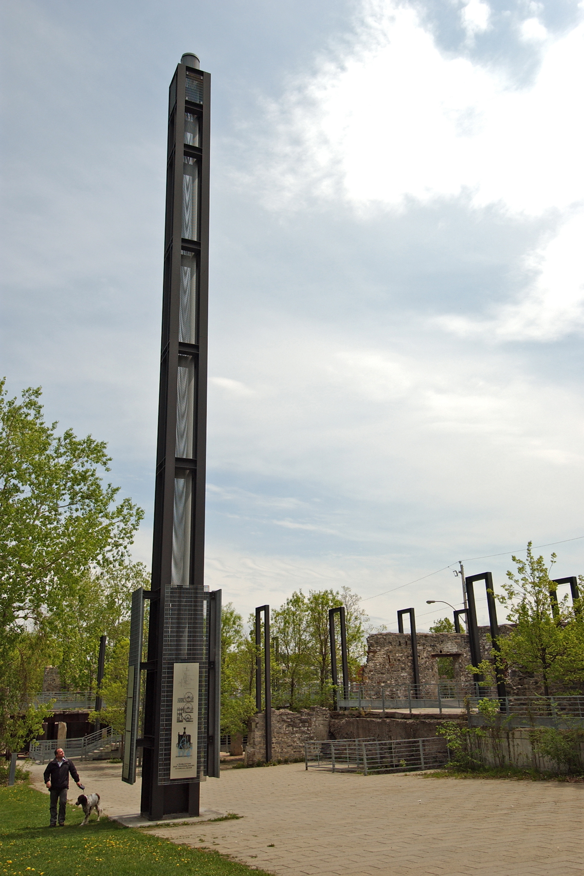 Man walks dog past old ruins and a tall metal structure in a park in Montreal