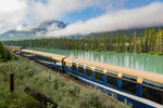 Rocky Mountaineer SilverLeaf train travels along Bow River and scenic landscape with tall trees and mountains