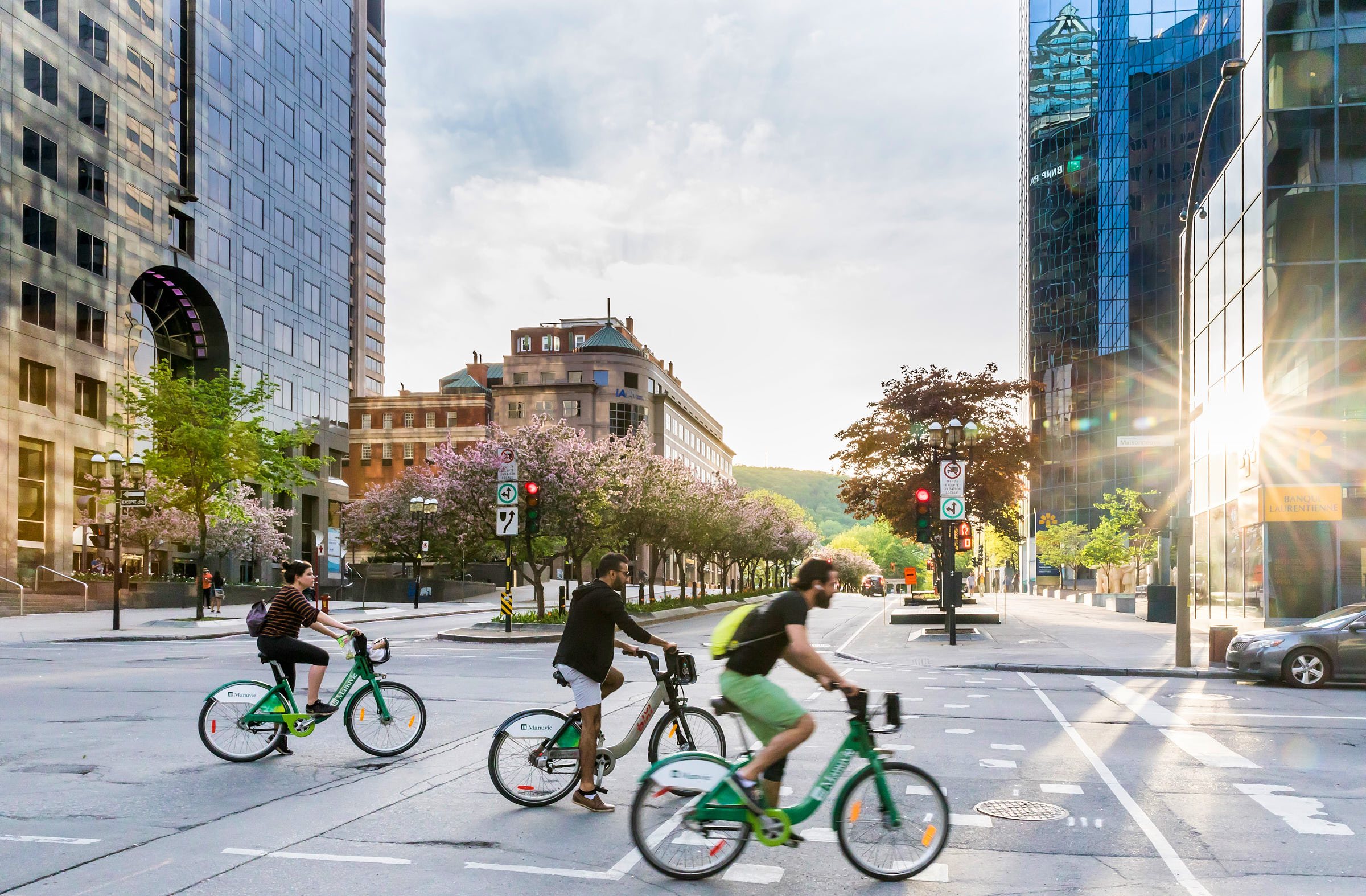 Three people biking in downtown Montreal with sun reflecting off of a building
