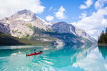 A person in a red canoe paddling across a bright blue lake in Jasper