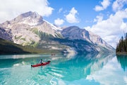 Person paddles a canoe across a lake in the Canadian Rockies in summer.