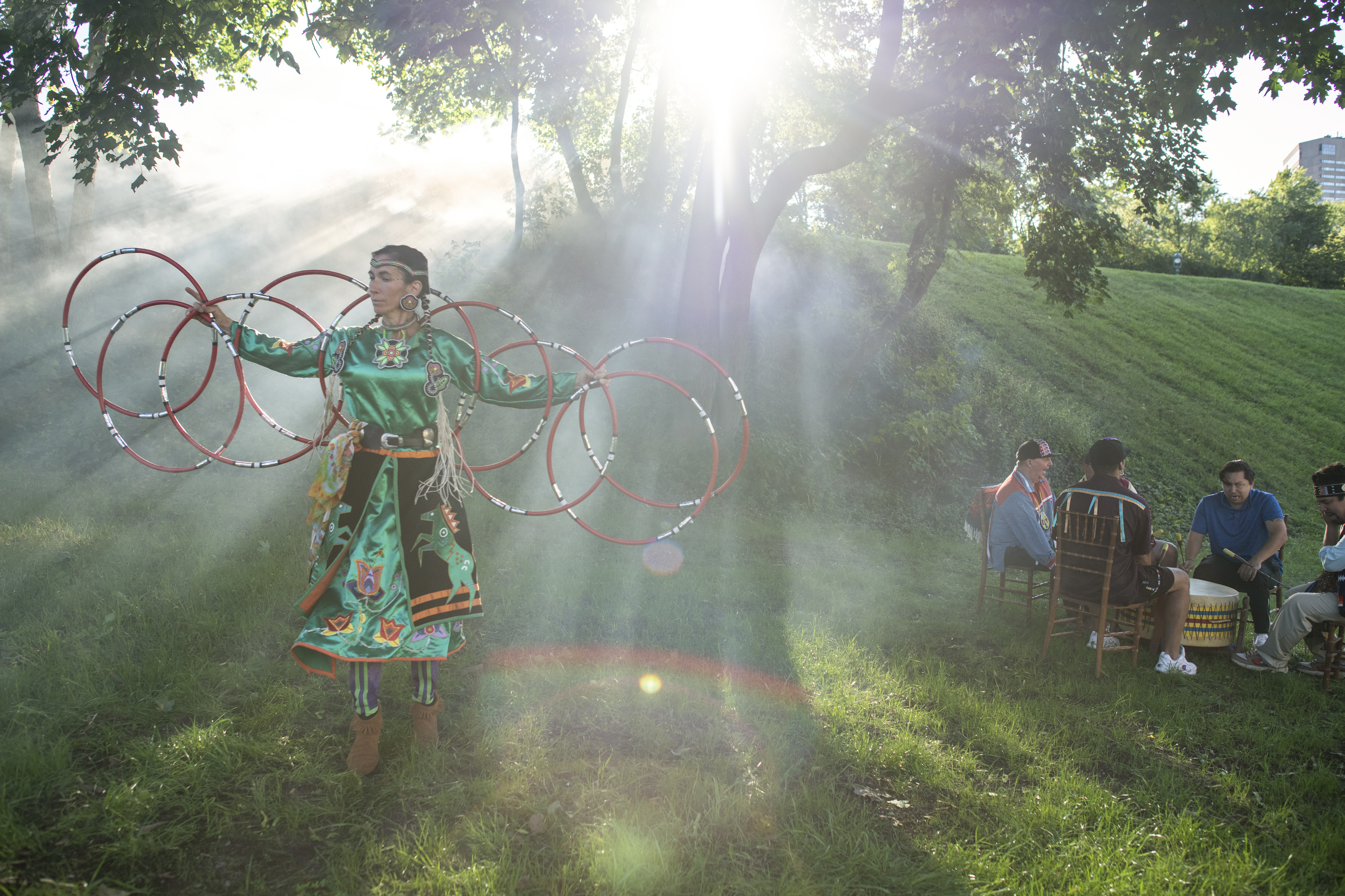 An indigenous artist performance in a park as a group sits behind