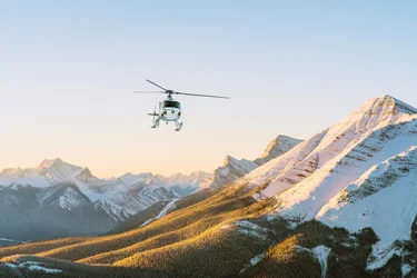 Helicopter flies over the rocky mountains at sunset