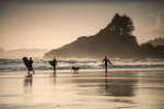 A group of surfers walk across a sandy beach in Tofino