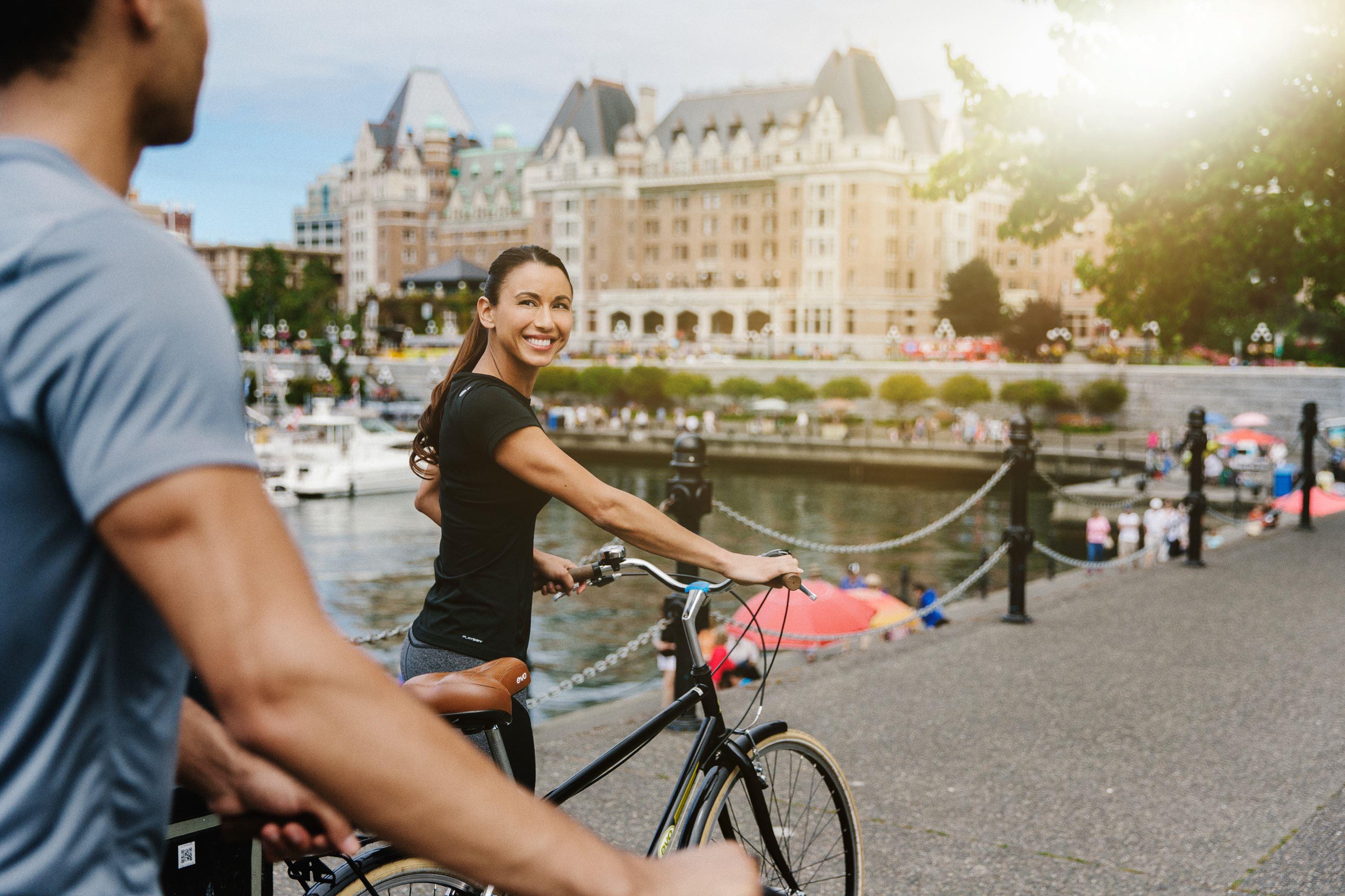 Girl holding a bike looking back at a man while standing in front of the Fairmont Empress in Victoria