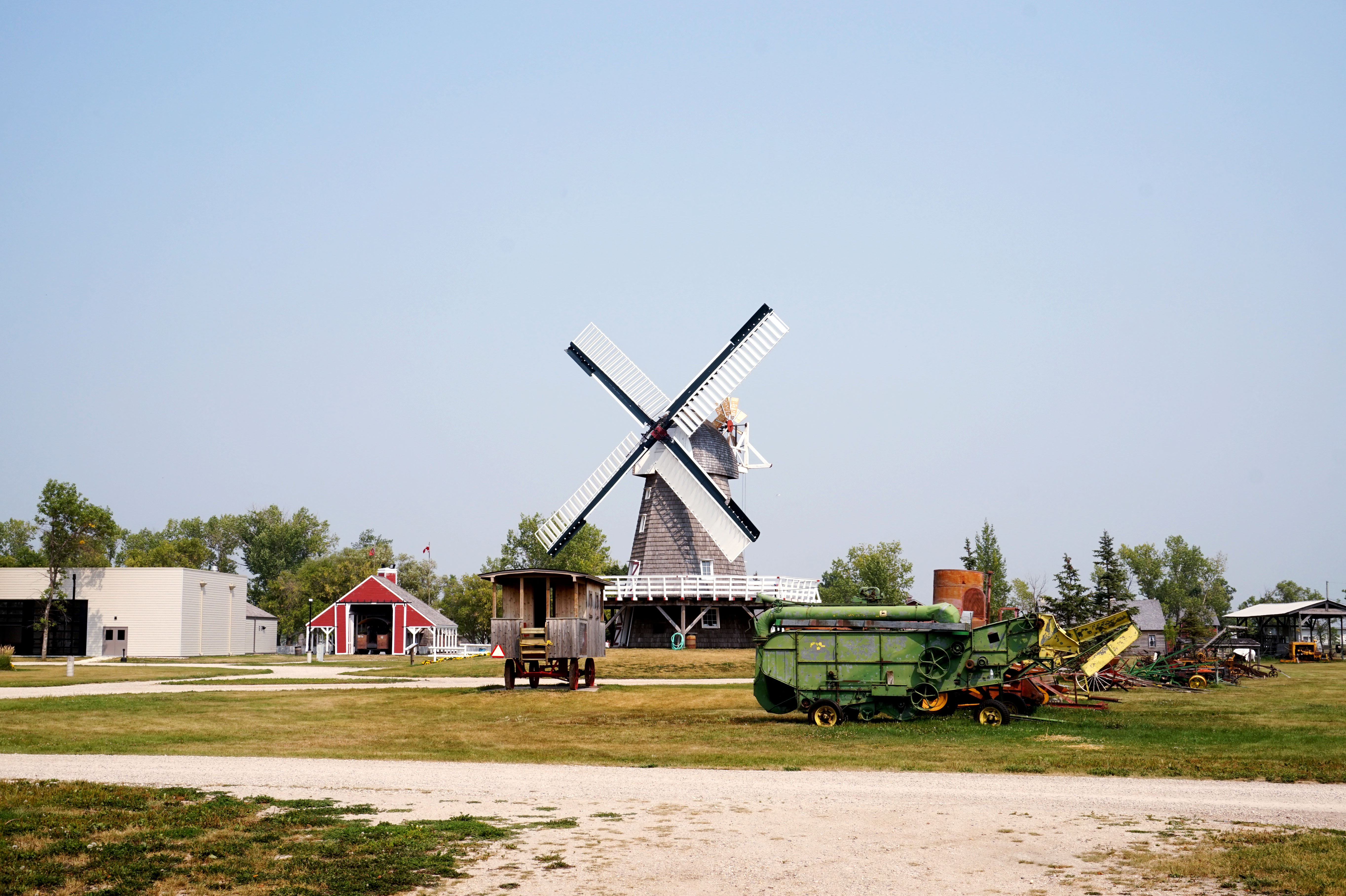 A windmill, red barn and old farm machinery on a field at the Mennonite Heritage Village