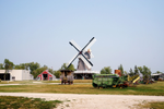 A windmill, red barn and old farm machinery on a field at the Mennonite Heritage Village
