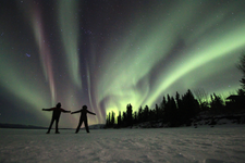 Two people on a frozen lake enjoying the northern lights in the Yukon