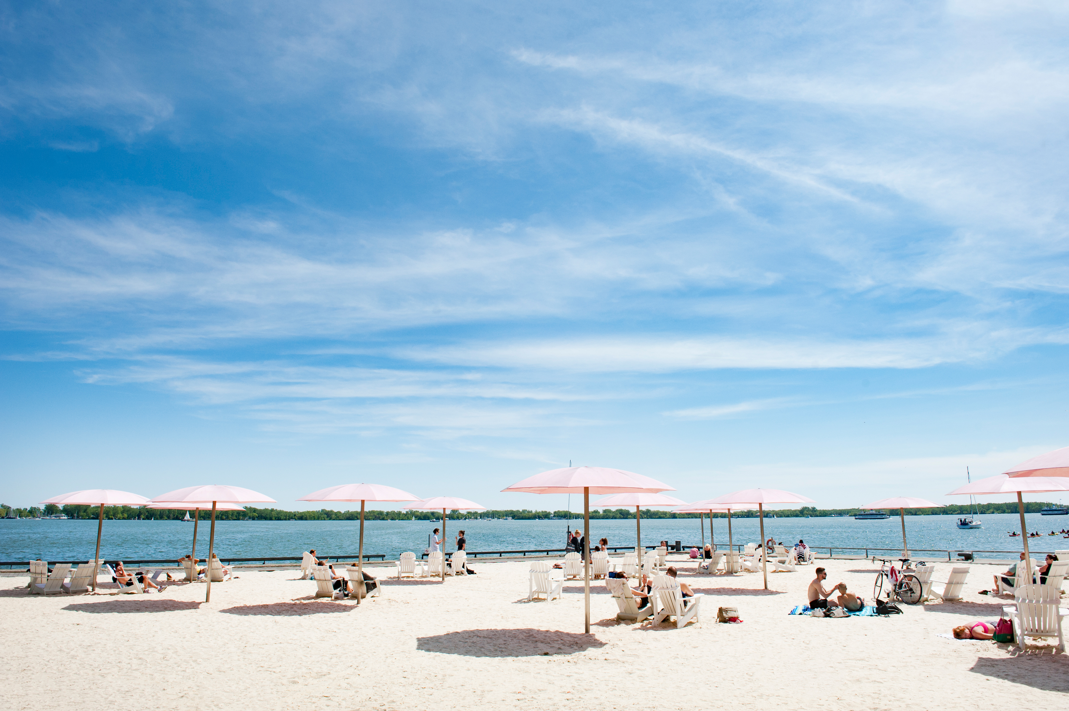 People sitting under pink umbrellas at the Sugar Beach waterfront area in Toronto