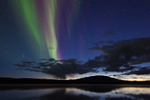 Aurora borealis appear across the sky like ribbons in the sky over horizon with vast body of water and silhouette of Mountains 
