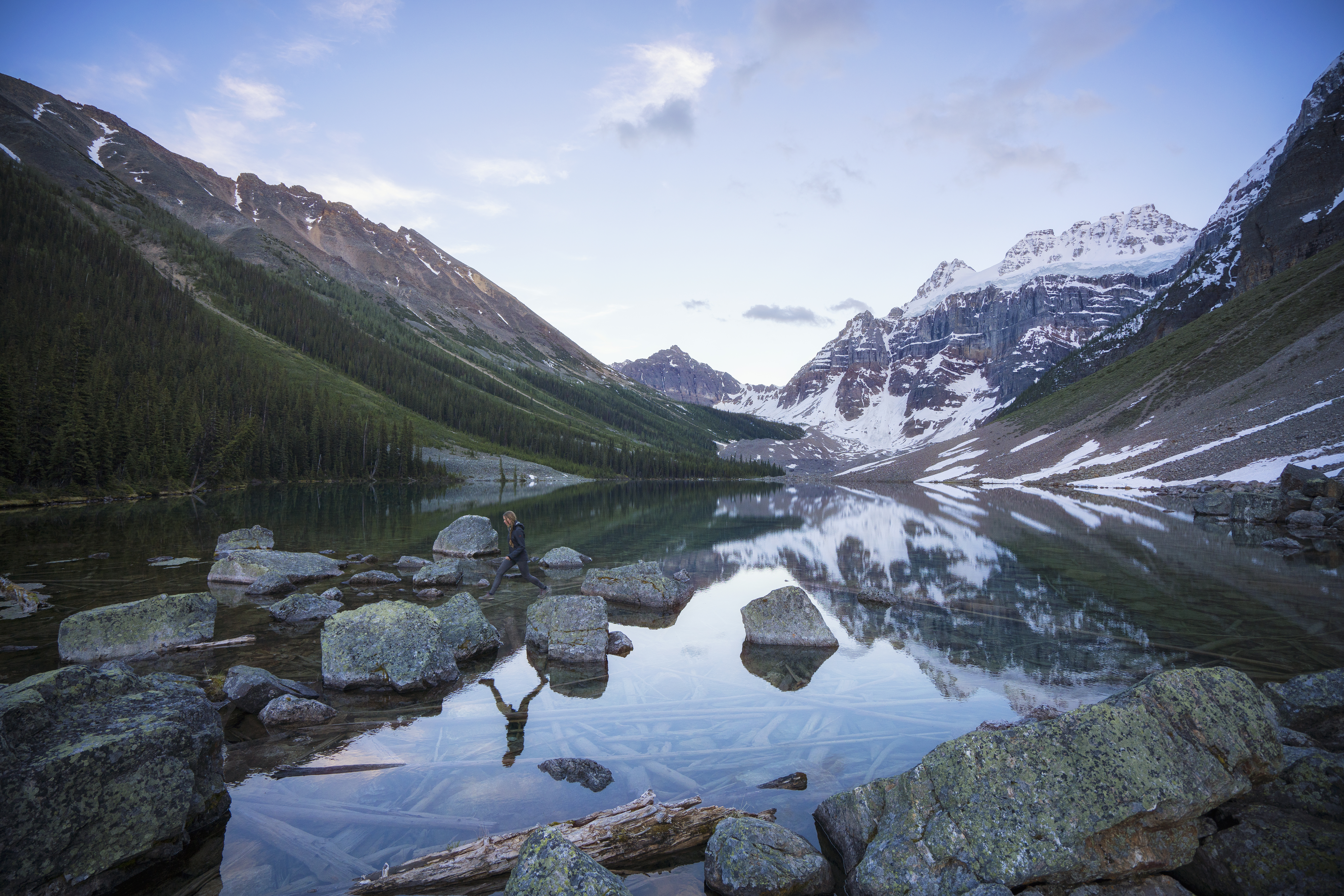 A person walks across rocks on the clear waters of Consolation Lake