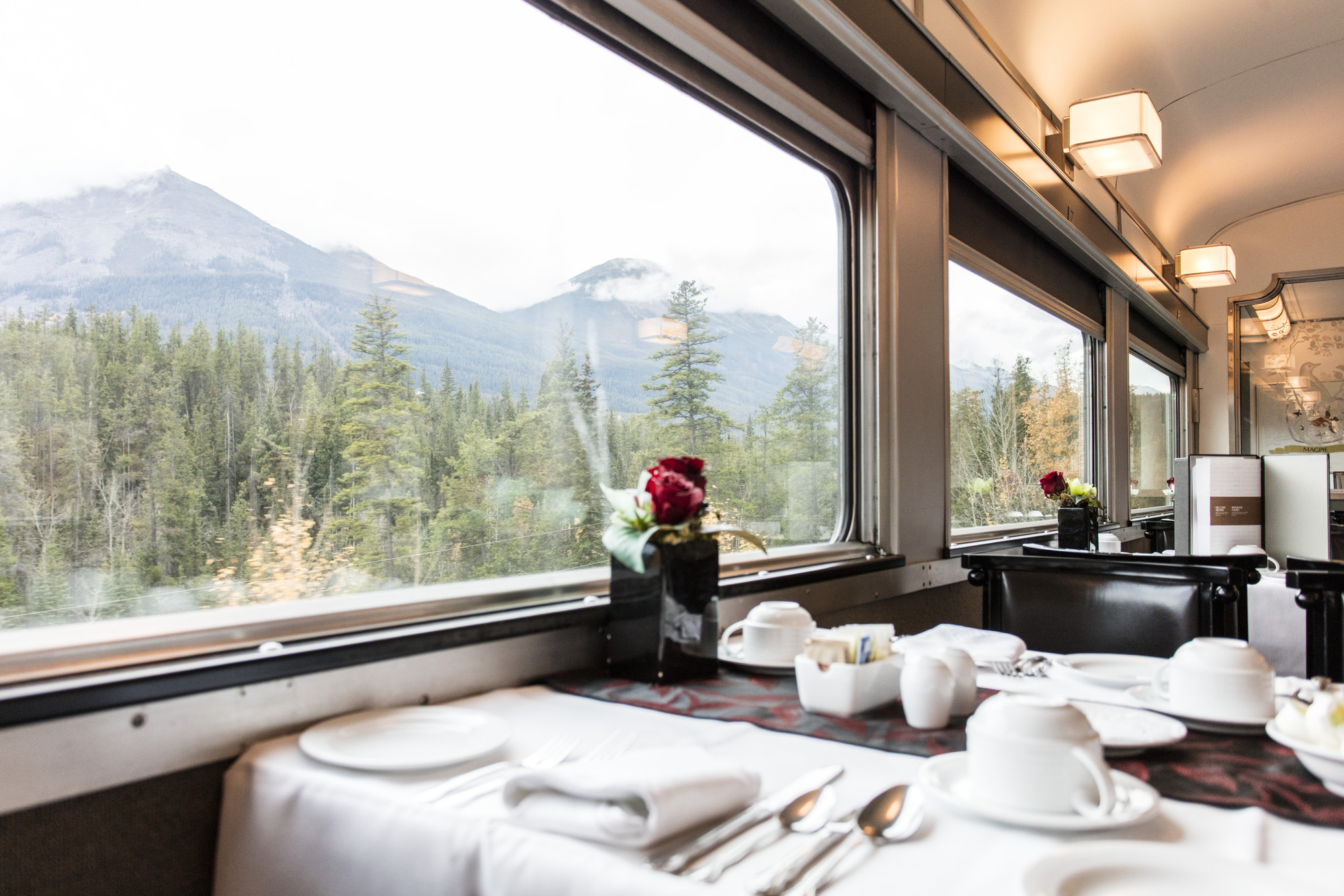 Closeup of a set table in the dining car with a mountain view in the background.