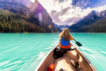 Woman paddles forward in Lake Louise in canoe towards mountains