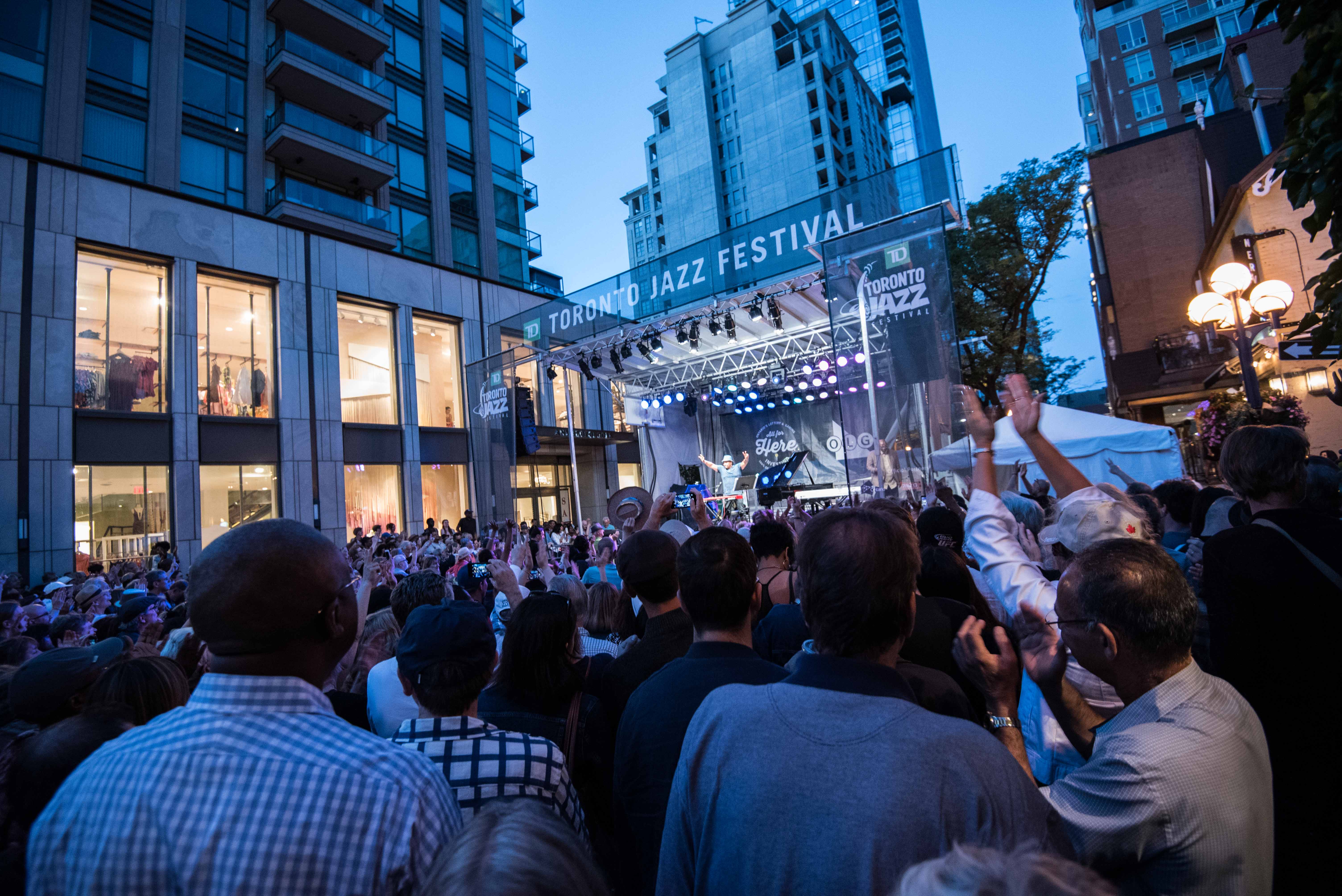 Audience watches a performer on the outdoor Toronto Jazz Festival stage at night
