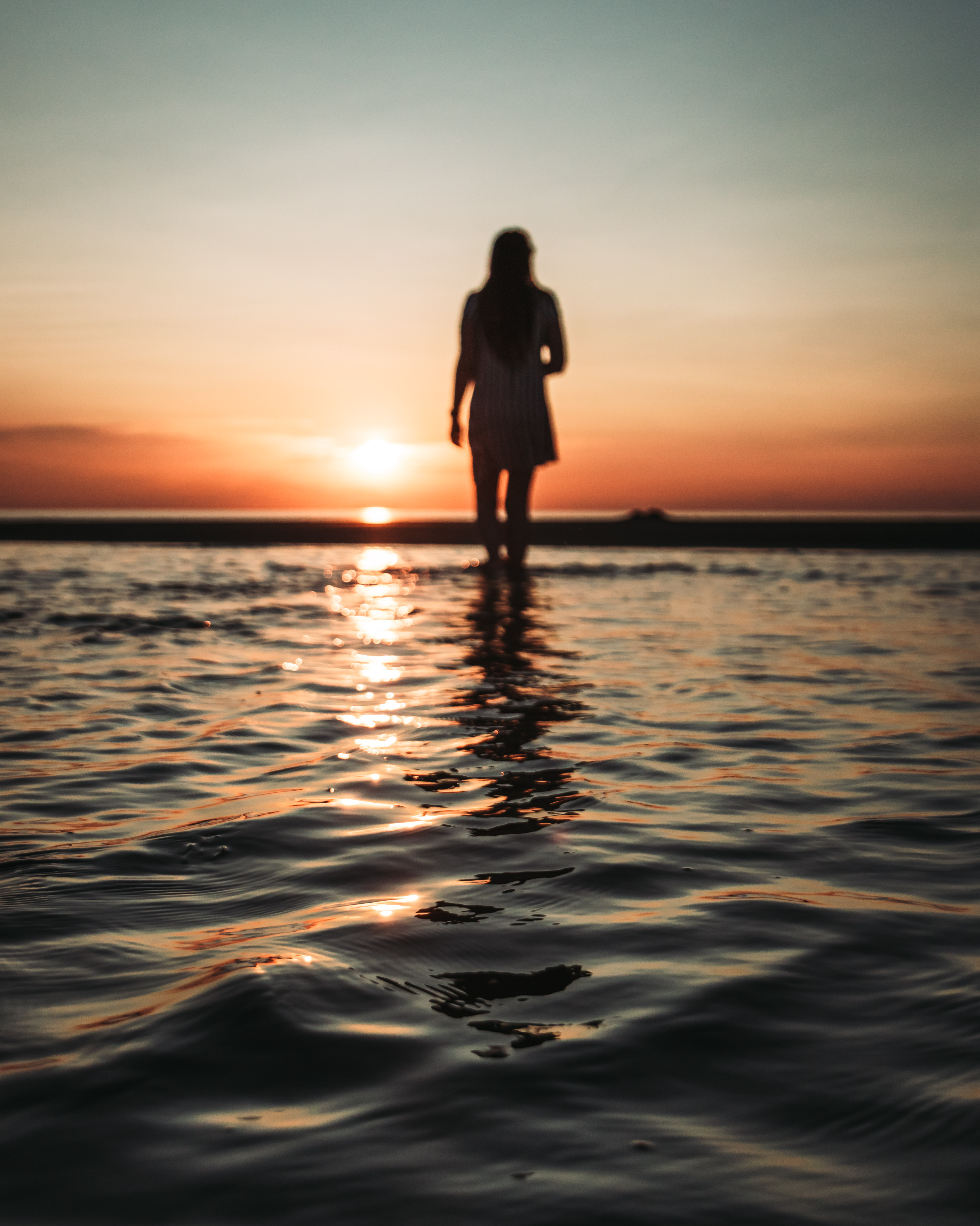 Woman faces horizon and stands in shallow saltwater of Aboiteau Beach at sunset