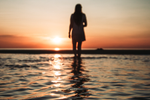 Woman faces horizon and stands in shallow saltwater of Aboiteau Beach at sunset
