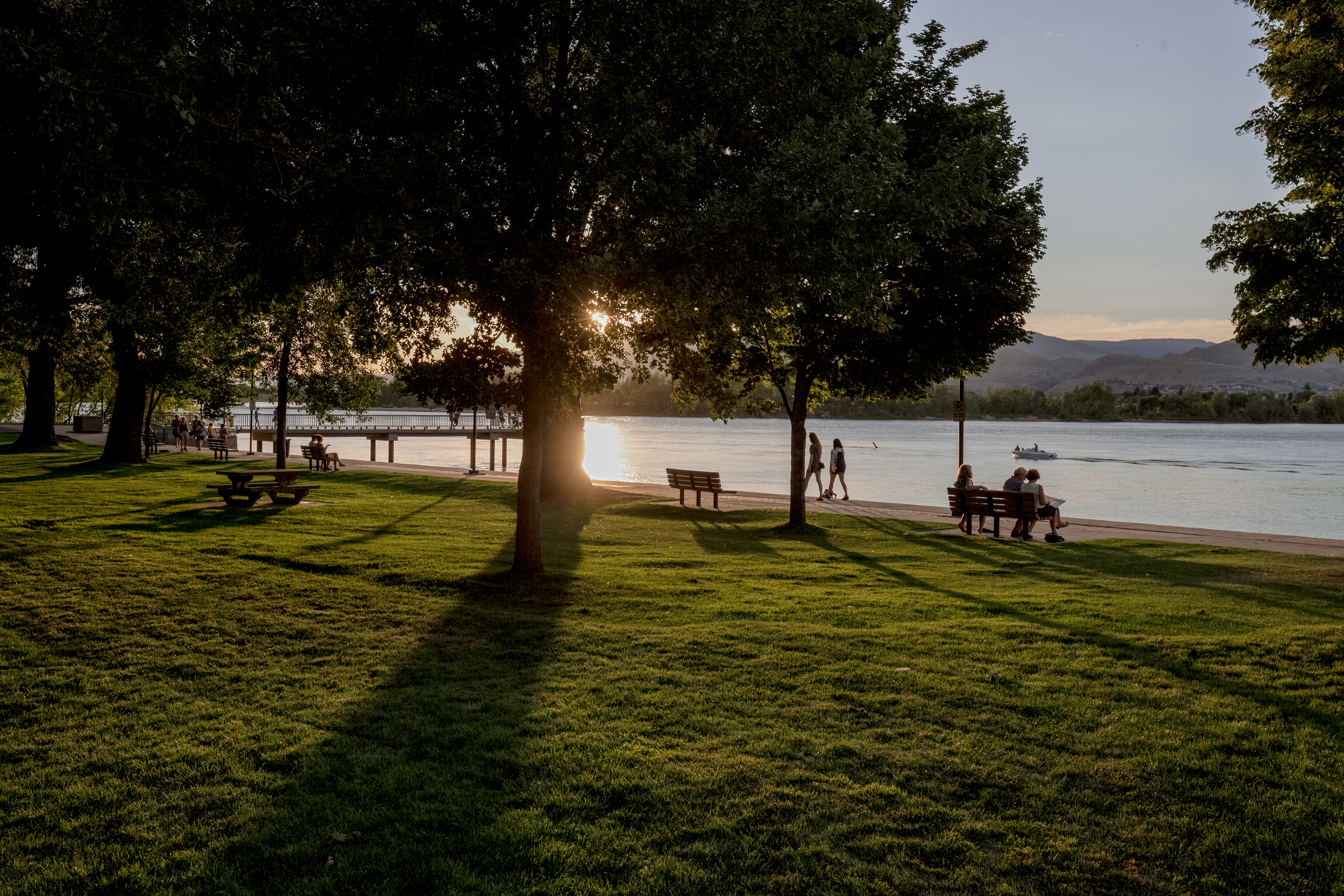 People sit on a bench looking out at the lake as the sun sets in Kamloops