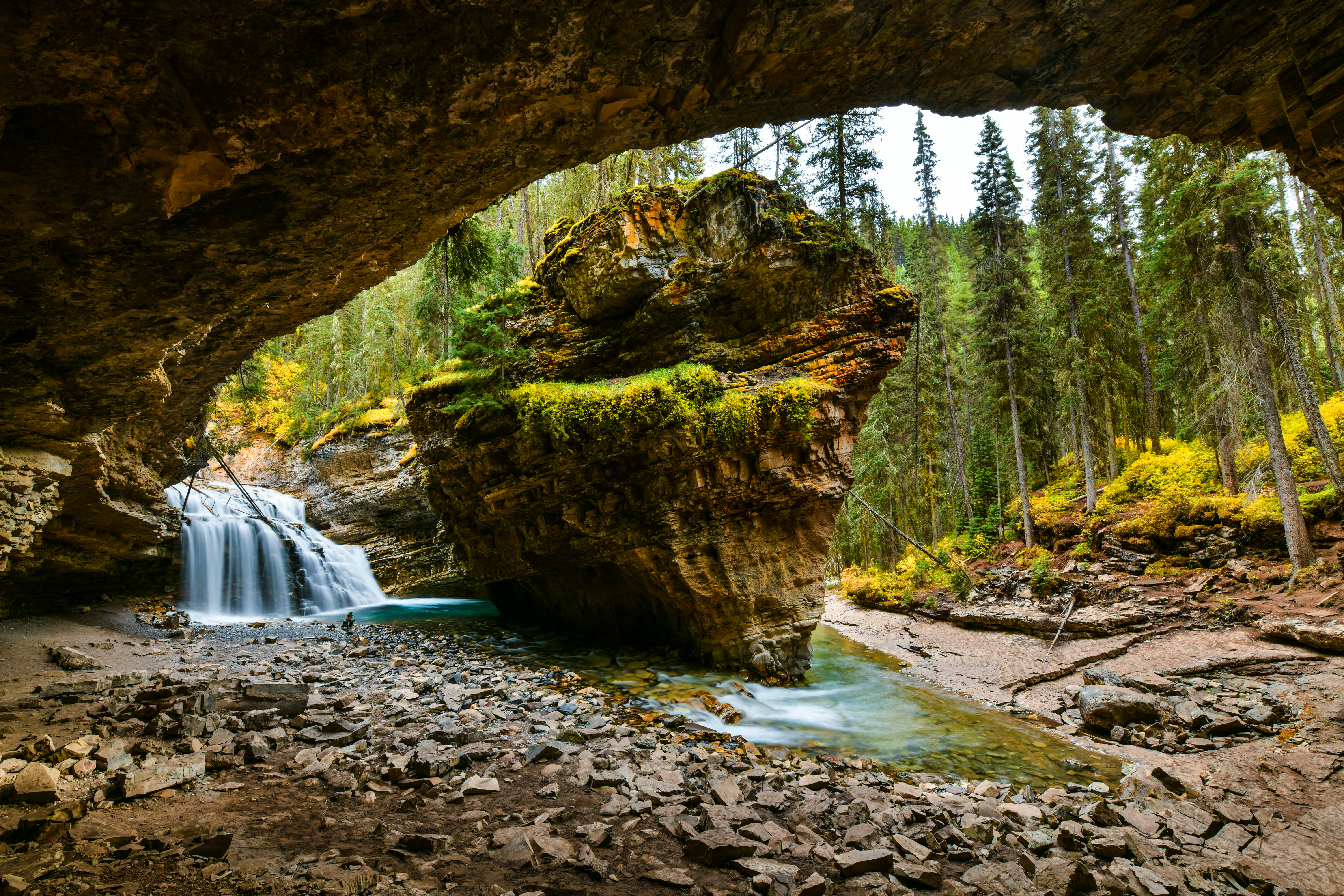 Lush and eroded limestone rock fixture stands in shallow pool by waterfall