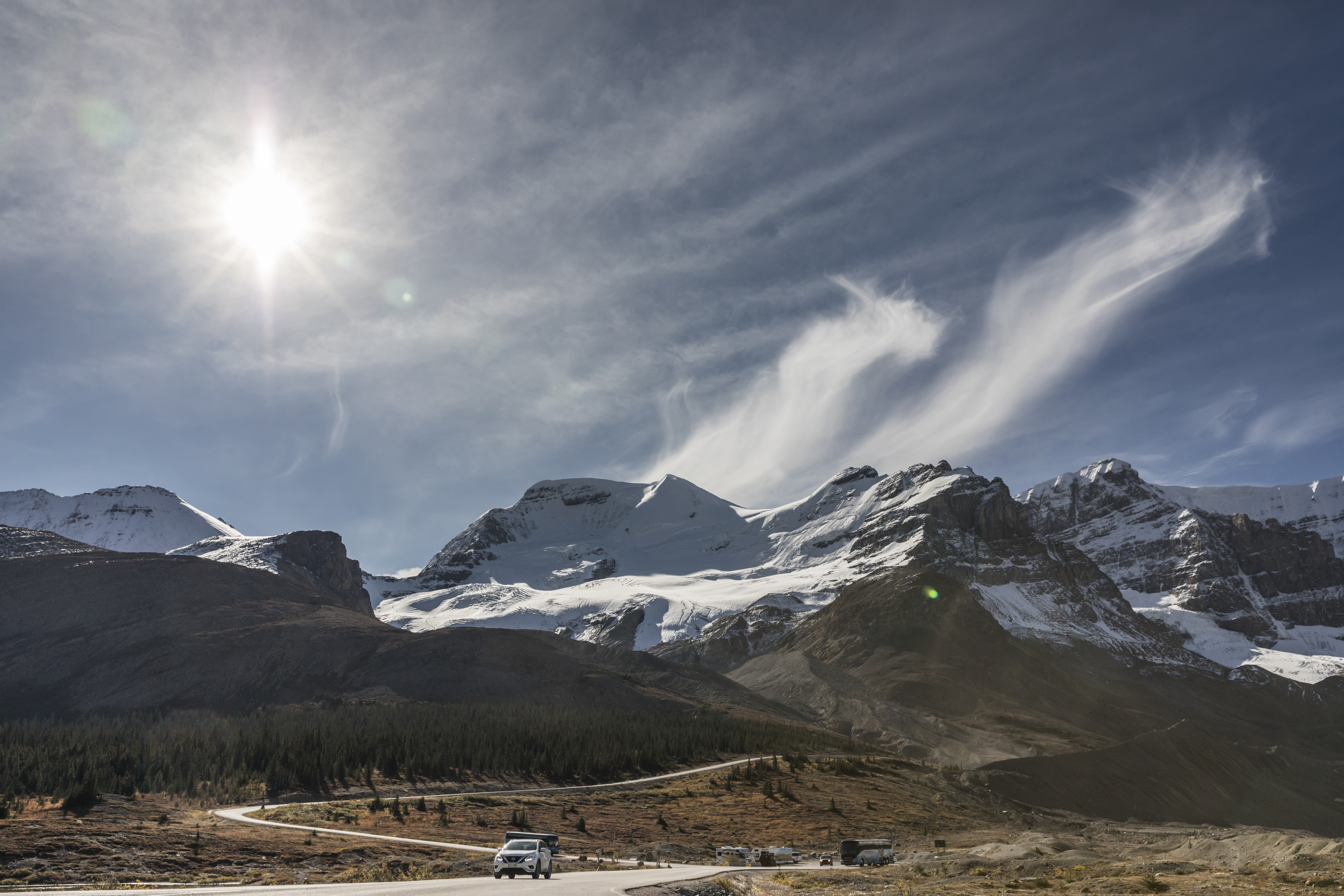 A car travels along the Icefields Parkway as glaciers and mountains loom in the background