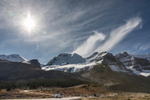 A car travels along the Icefields Parkway as glaciers and mountains loom in the background