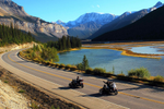 Two motorcycles with sidecars drive past a lake and mountains in Jasper National Park 