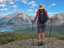 Woman standing with hiking poles overlooks a mountain and lake.