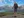 Woman standing with hiking poles overlooks a mountain and lake.