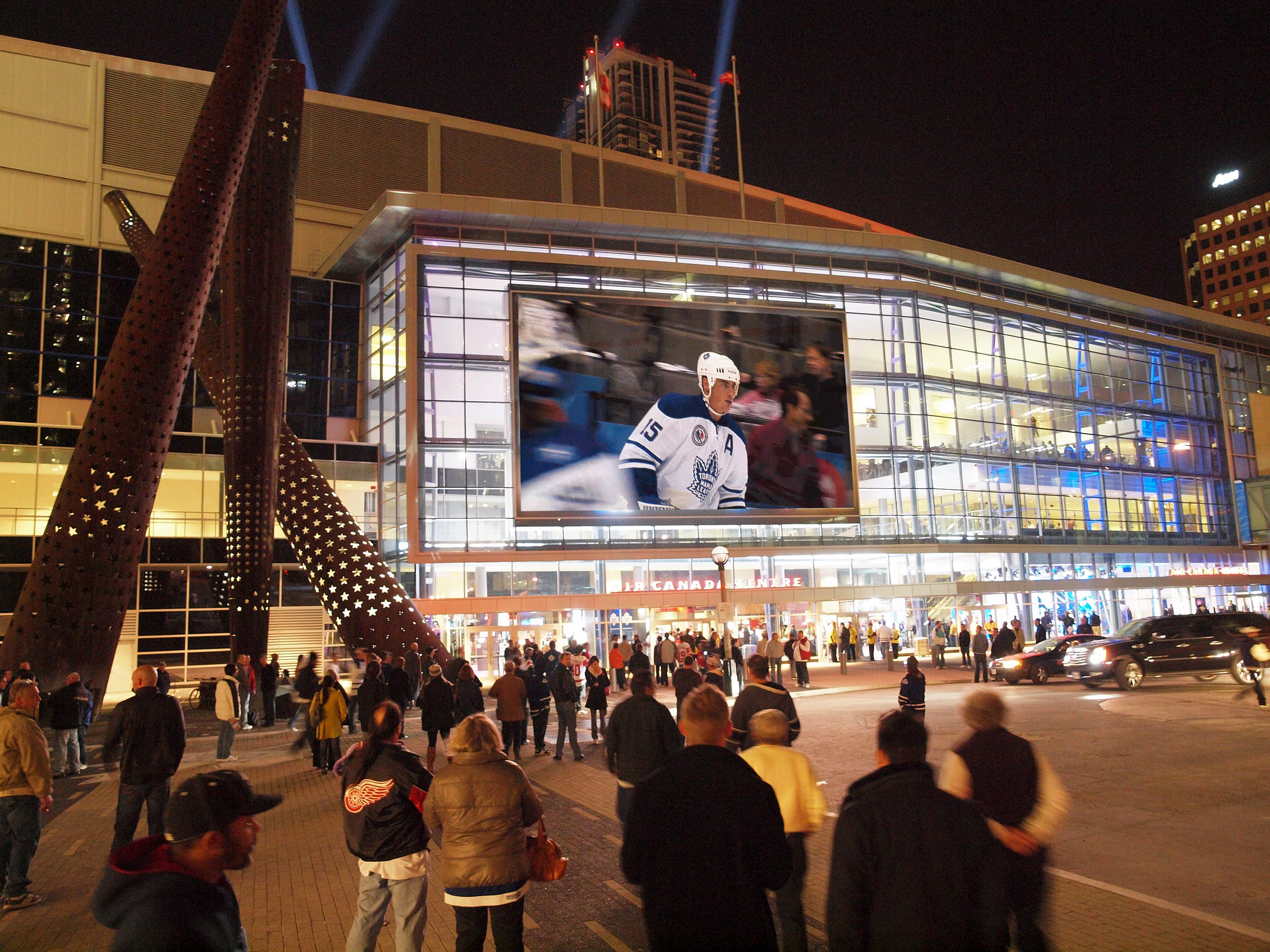 Crowds of people outside of the Scotiabank Arena while a Toronto Maple Leafs NHL hockey game plays on a large digital screen