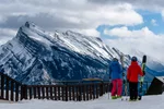 Two skiers standing at a fence, looking out over Mount Norquay in Banff